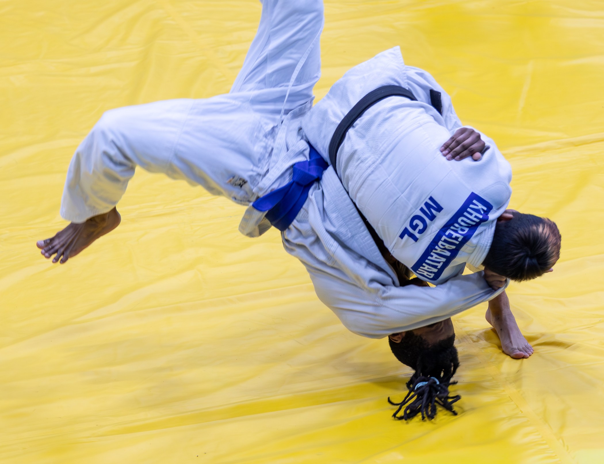 Two judoka mid-throw on a yellow mat